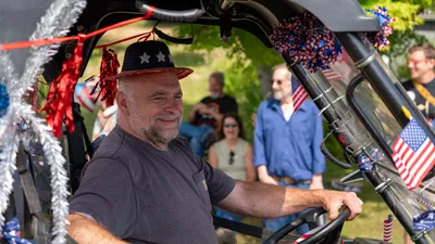 A man in a patriotic hat grins from the seat of a decorated vehicle during the Fourth of July parade in Home, Washington.